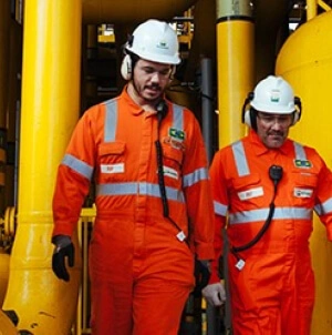 Dois homens lado a lado, ambos usando uniforme laranja da Petrobras.
