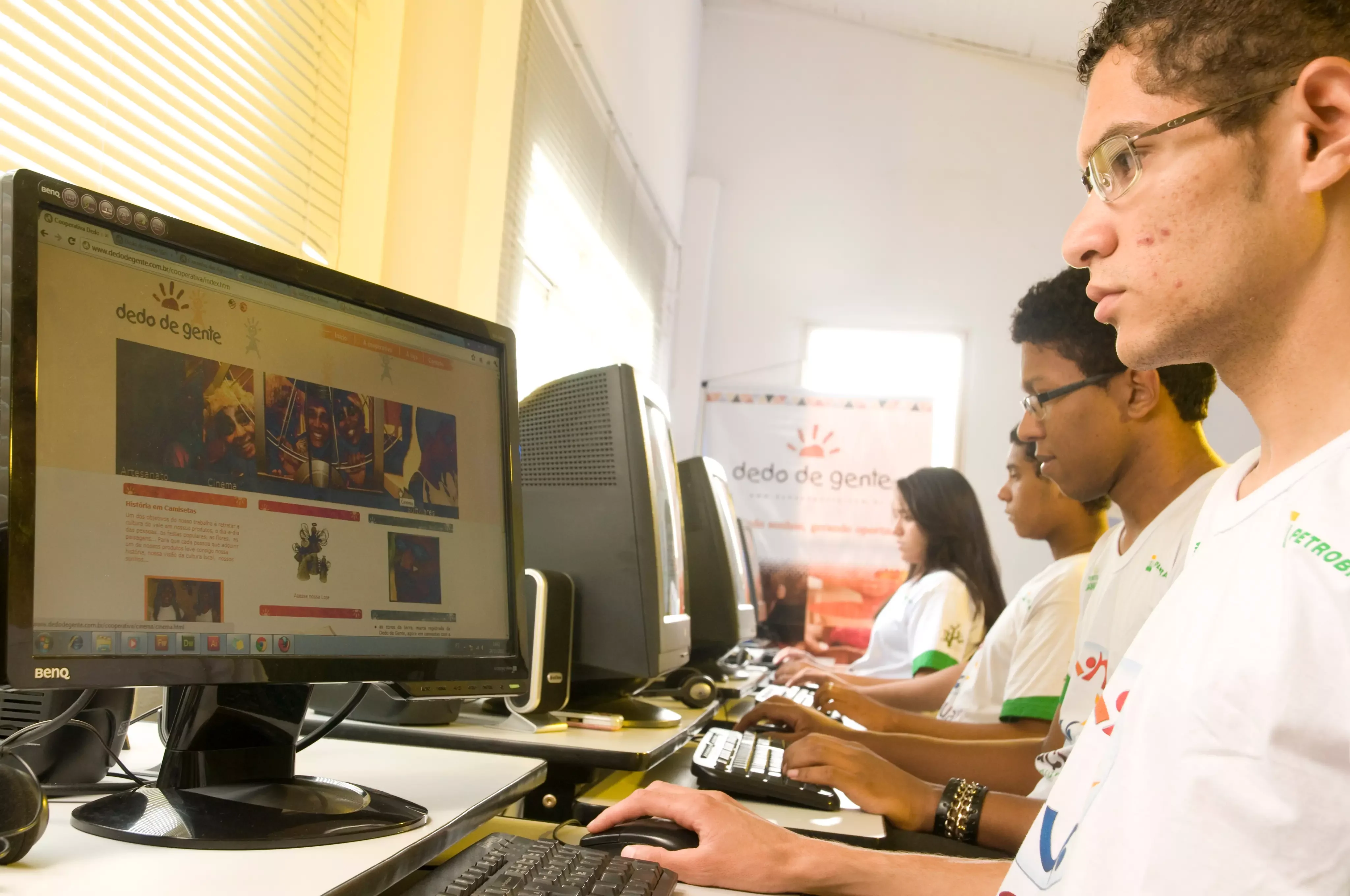 Quatro adolescentes enfileirados mexendo em computadores em laboratório.
