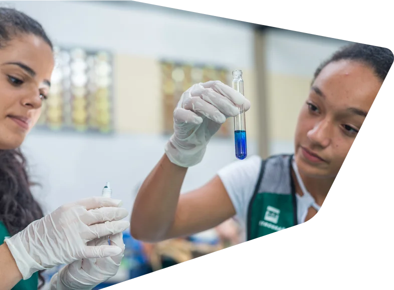 Duas mulheres realizando experimentos. Uma delas segura um tubo de ensaio com um líquido azul.