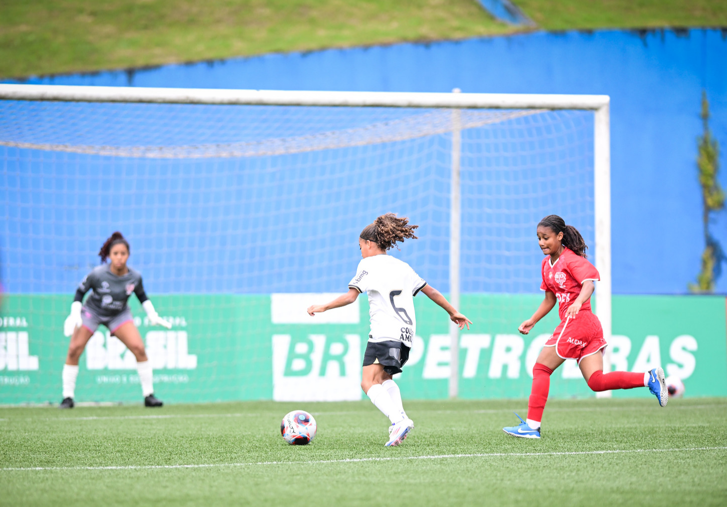 mulheres jogando futebol com placa de campo com logo Petrobras