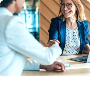 Two people shaking hands across a desk during a business meeting.