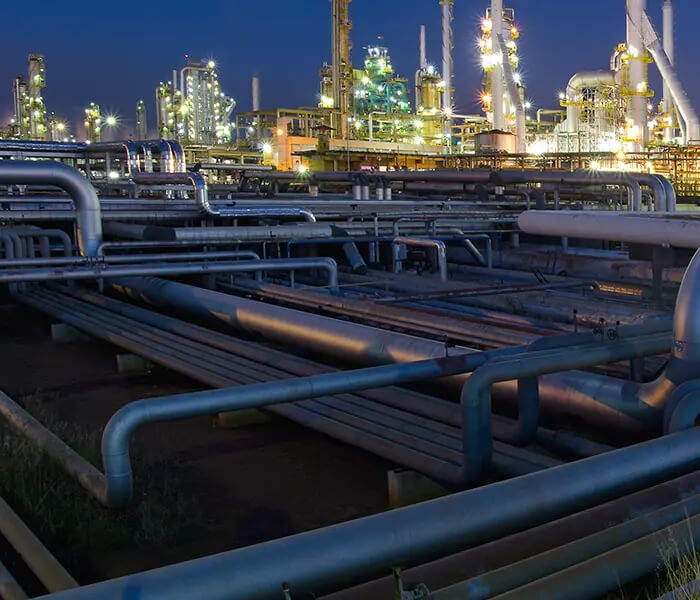 dutos com uma refinaria iluminada ao fundo